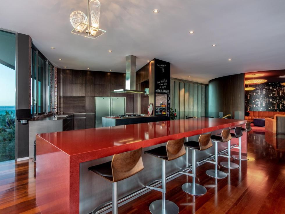 A high-end kitchen with a stone island bar, dark timber cabinetry and sea views